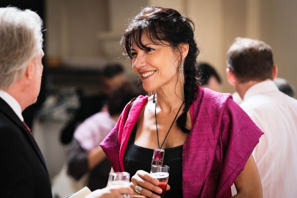 femme brune souriante avec une frange et une natte qui porte une étole rose
