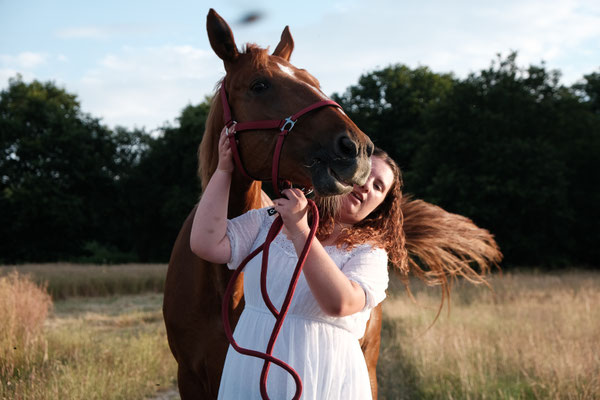 femme en robe blanche qui tient la tête de son cheval