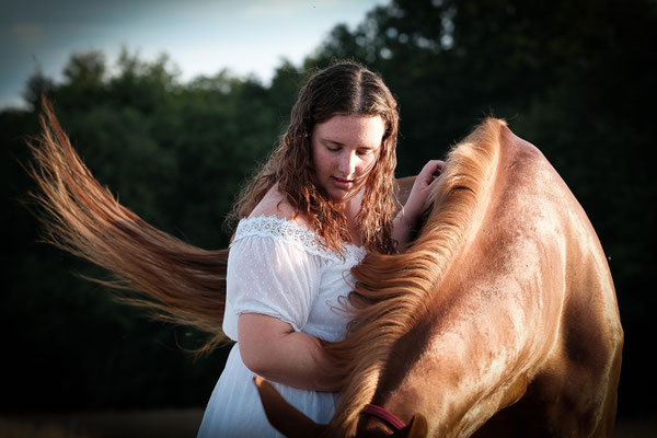 femme qui caresse son cheval qui bat l'air avec sa queue