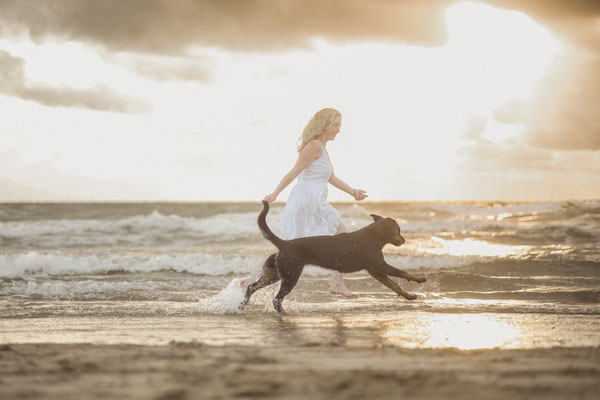 Frau im kleid rennt mit ihrem Hund am Meer, Julianadorp