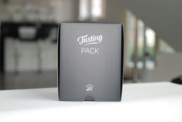 Eine Kartonverpackung ist zu sehen. Die Verpackung besteht aus Karton, ist dunkelgrau und es handelt sich um eine Frontal-Aufnahme.