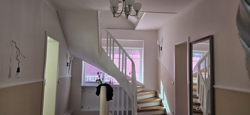 Renoviertes Treppenhaus mit Flur in einem Einfamilienhaus, helle Wandgestaltung in Beige und Creme, getrennt durch weiße Stuckleiste, kombiniert mit warmem Parkettboden.
