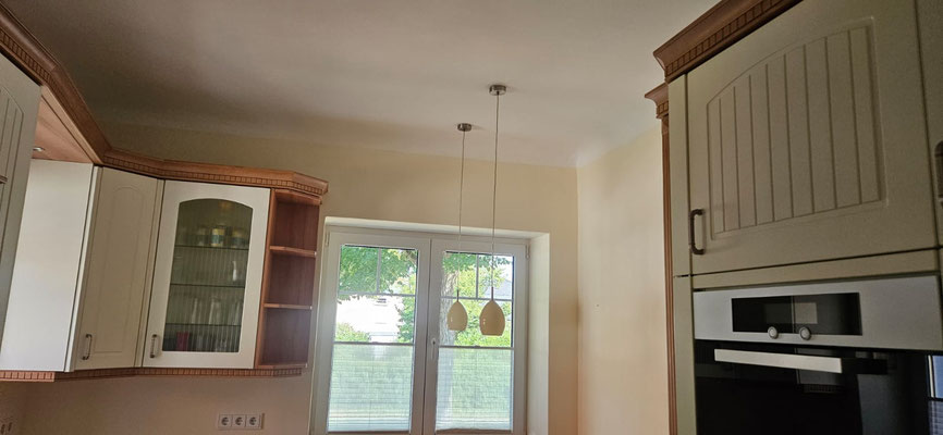 Heller Küchenraum mit Landhaus-Charme, Wände in sanftem Gelb, Decke und Fensterumrandungen klassisch weiß.