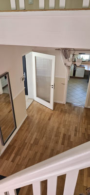 Modern renoviertes Treppenhaus mit Flur: warme Parkettböden, abgestufte Wandfarben in Beige und Creme, elegant getrennt durch weiße Stuckleiste.