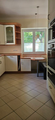 Heller Küchenraum mit Landhaus-Charme, Wände in sanftem Gelb, Decke und Fensterumrandungen klassisch weiß.
