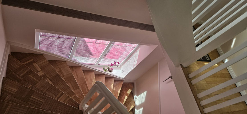 Helles Treppenhaus im Einfamilienhaus nach Renovierung: untere Wandhälfte in Beige, obere in Creme, weiß abgesetzt, Parkettboden und angepasste Treppenstufen.