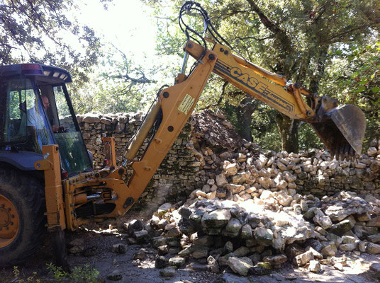Première étape : intervention au tracto-pelle pour faire tomber le couronnement cimenté. Un coup de godet et le reste du parement s'écroule comme un château de cartes