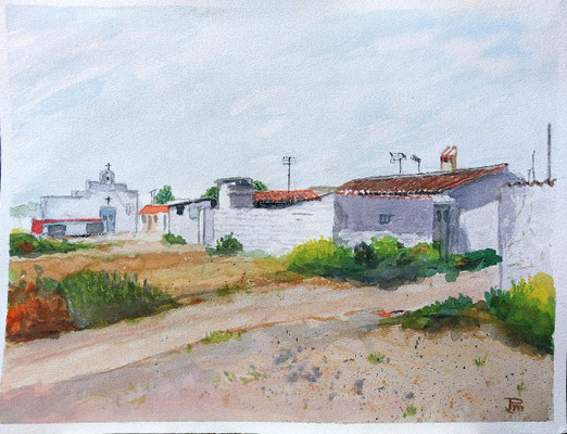Casas blancas con tejados rojizos, camino de tierra, vegetación baja y una iglesia al fondo bajo cielo suave.