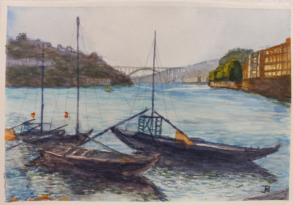 Barcas amarradas en un río amplio, con colinas, edificios y un puente al fondo.