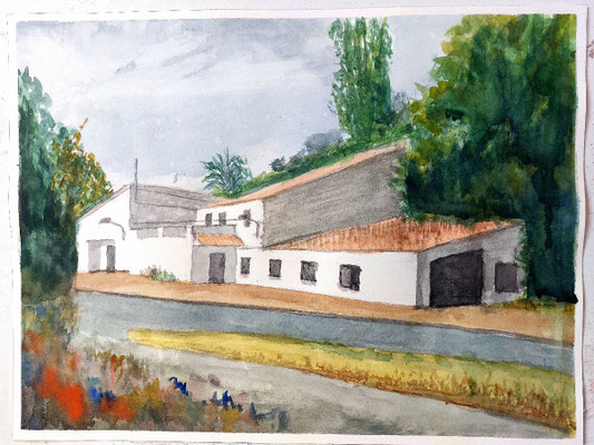 Alquería blanca con tejados rojizos, árboles altos detrás y camino rural en primer plano.