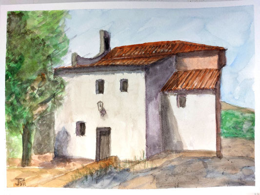 Ermita blanca con tejados rojizos, puerta oscura, árbol frondoso a la izquierda y colinas suaves al fondo bajo cielo claro.