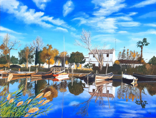Barcas amarradas en el puerto de Catarroja con reflejos en el agua, vegetación y la Casa Zulema al fondo.