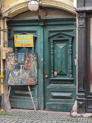 Eine alte Haustür mit Bild auf Staffelei und Schild "Änderungsschneiderei im Hof"