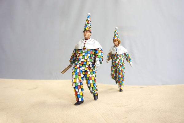 Miniaturpark "Die Kleine Sächsische Schweiz" Schifferumzug, 15cm. Das Bild zeigt zwei Personen in lustigen Kasperle-Kostümen. Sie sind bestückt mit etlichen bunten Wimpeln. Sie tragen hohe Spitzhüte und Holzklappern.