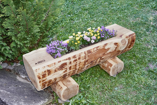 Bepflanzter Blumentrog aus Lärchen-Rundholz mit Splint und Holzfüssen in Seitenansicht.