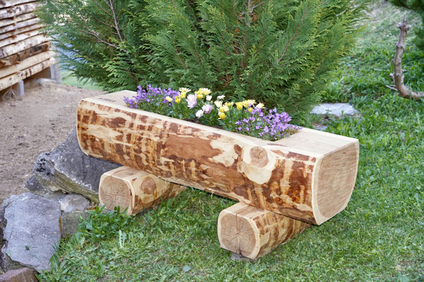Bepflanzter Blumentrog aus Lärchen-Rundholz mit Splint auf Holzfüssen im Garten.