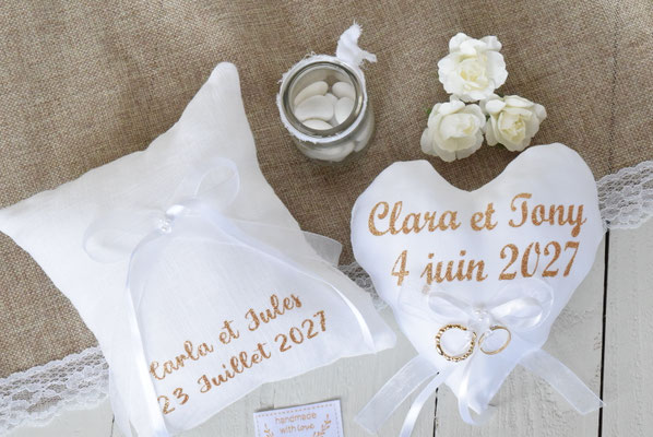 deux coussins porte alliances pour amriage, en lin carré personnalisé avec prénom et date mariage, et un autrer coussin en forme de coeur en satin balnc et dentelle, personnalisée avec les prénoms et date de mariage en doré