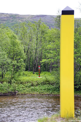 Im Vordergrund an einem Ufer des Jakobselva steht der norwegische gelbe Grenzpfahl, nur weniger Meter am anderen Ufer der russische in grün-rot