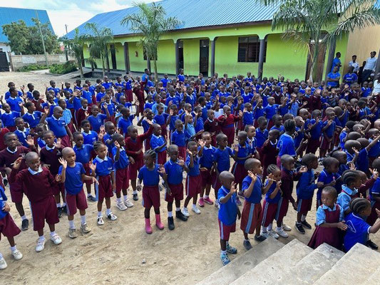 Eine Schulgruppe in blauen Schuluniformen bei einer kleinen Begrüßung vor dem Gebäude