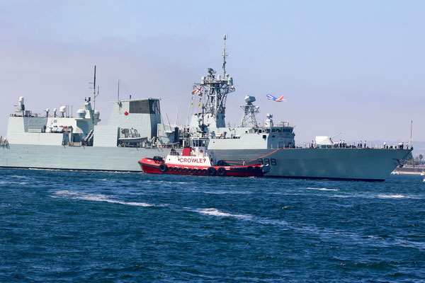 Zwei Schlepper bringen ein Kriegsschiff in den Hafen.