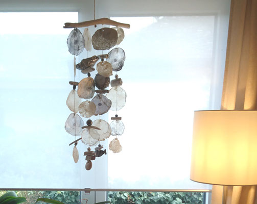 Dekoidee: Als Fensterschmuck ein Muschelwindspiel in grau-weiß neben einer Stehlampe.