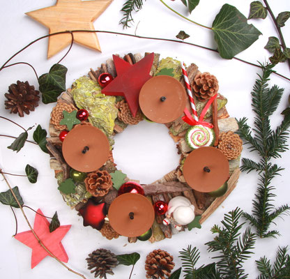 Tischholzkranz aus braunen Treibhölzern und grüner Rinde mit roter weihnachtlicher Dekoration.