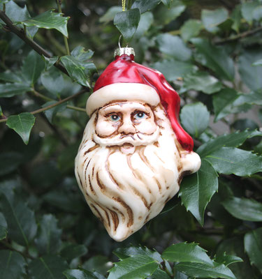 Weihnachtsmanngesicht mit weißem Bart und roter Mütze aus Glas als Christbaumschmuck.