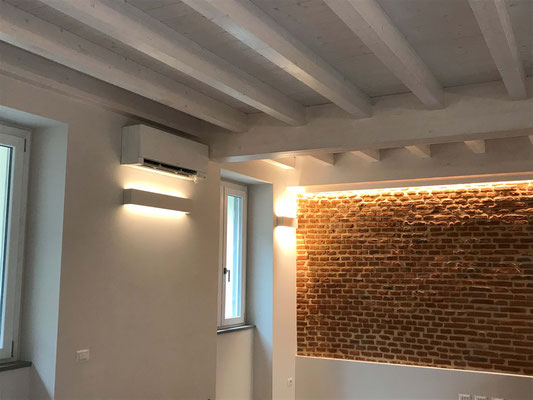 Angolo soggiorno con lampade su disegno e parete in mattoni illuminata da striscia led