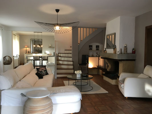 Ambiance sereine et naturelle pour ce grand séjour beige et blanc ouvert sur une cuisine et un escalier.