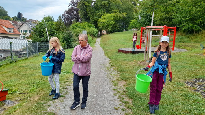 Zwei Schülerinnen sammeln mit ihrer Lehrerin Müll im Park