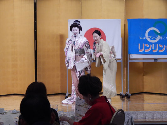 第一ホテル東京「ラ・ローズ」のステージにて、着物姿の林佑樹様と渡邊さゆりがマイクを手に来場者へ挨拶している様子。背後には金屏風と隣々会UNIONの旗が飾られている。