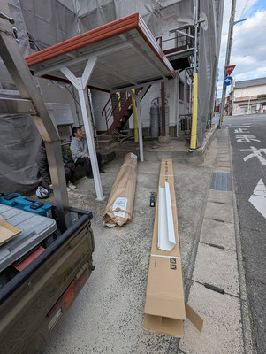 2025年2月11日（火）午後3時過ぎ　休憩している職人さんたち。缶コーヒーを手に（hotだと思います）話が弾んでいました。資財は右側の大きいのが横に取り付ける雨樋（近くで見ると雨どいの幅とか深さは、従来のものの3倍はあります。大げさではありません）。左側は「縦」に取り付ける雨樋だそうです（大雨を受けとめる必要なく細くてもよいのです）。