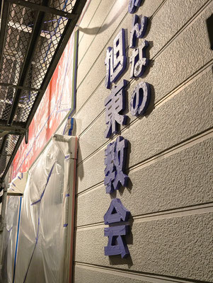 2024年12月18日（水）午後6時　外での片付けを牧師も終えて（枝の処理・ゴミ出し準備）会堂の壁面を見ると、いつも、緑色の「みんなの旭東教会」の文字が、アドヴェント・待降節の紫色に変身してました。いやいや、養生のテープが紫色なのでした。これはこれでなんだかとても美しいのであります。