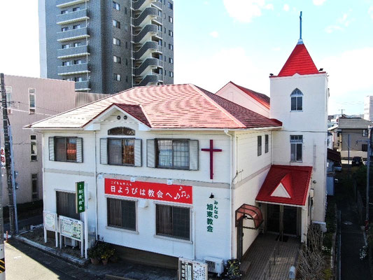 ※屋根工事の参考のためにここに普段のHPの場所から移動しています。屋根の正面真ん中にある三角形の部分、実は、ガルバリウム鋼板の鈑金が複雑に必要な箇所のようです。頭に置いて屋根工事の写真ご覧下さい。　2024年12月　表通りから見る旭東教会です。手前の建物は附属館です。1階は集会室。外壁塗装・屋根工事が始まる前に工事を依頼した業者さんがドローンで撮影されたもの。次の写真と比べるとわかりますが、普通には素人では撮影できない空からの一枚であることがわかります。