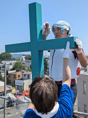 2024年8月3日（土）いよいよ十字架の設置工事も最終盤です。縦の柱に横棒が取り付けられていきます。牧師の森もヘルメットを被り38度の屋上に上り撮影です。