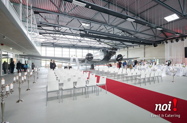Viele gedeckte Tische befinden sich in einem Flugzeughangar neben einer JU 52. © noi! Event & Catering CmbH & Co. KG