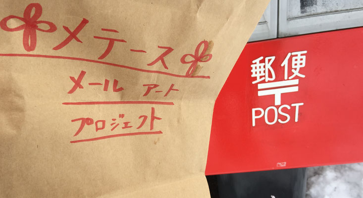 封筒は茶色の紙袋に入れて運びます。そこにはメテース メールアート プロジェクトと赤文字で記載されています。The envelopes are carried in a brown paper bag. It is marked on it in red letters as the Metace Mail Art Project.