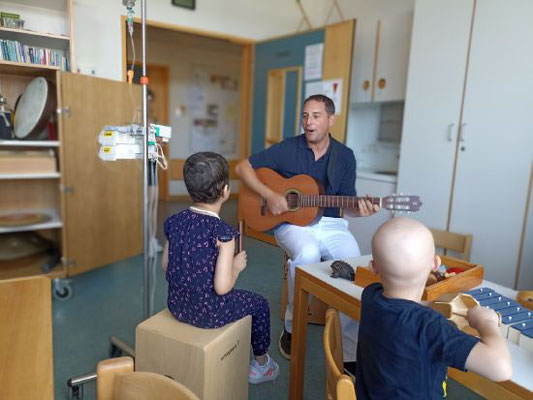Mann spielt mit Gitarre vor zwei Kindern