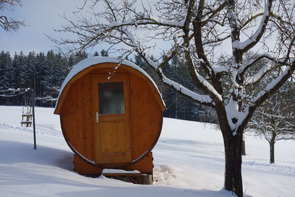 Schneebedeckte Fasssauna im Garten am Biohof Stadler