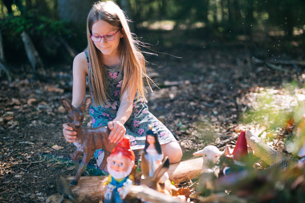 Ein Mädchen sitzt am Waldboden und spielt mit Gartenzwergen im Wald