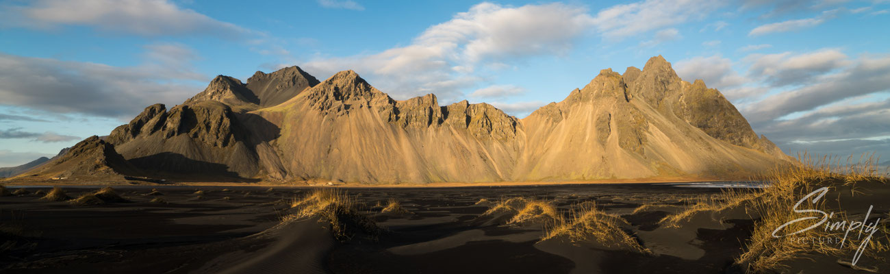 Schwarzer Strand mit blauem Himmel und leuchtend braunem Gras bei Stokksnes.