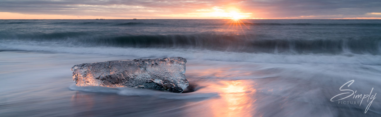 Sonnenuntergang mit einer schimmernden Eisscholle am Diamond Beach bei dem Jökulsárlón Glacier Lagoon.