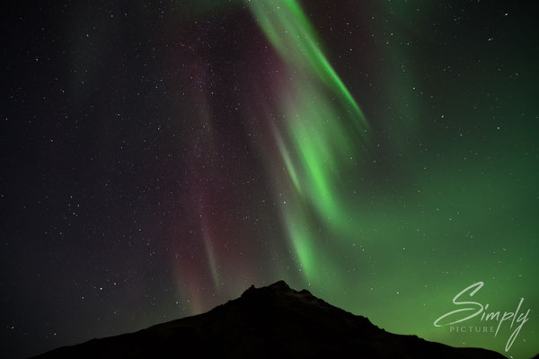 Nordlichter in grün und rot bei dem Skógafoss Waterfall.
