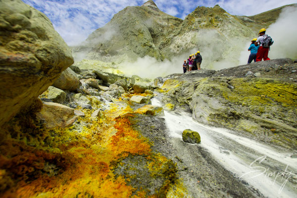 Whakaari, White Island, gelb-braun-rote Gesteine neben dem Weg mit Personen im Hintergund