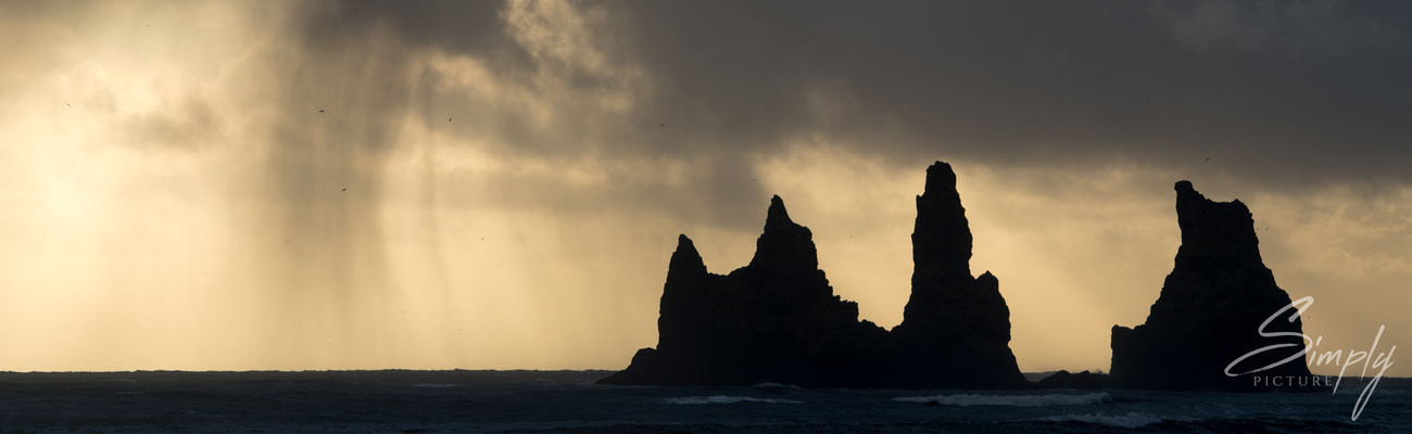 Spitzige Felsen im Meer mit goldiger Regenstimmung bei Reynisdrangar nähe Vík í Mýrdal.