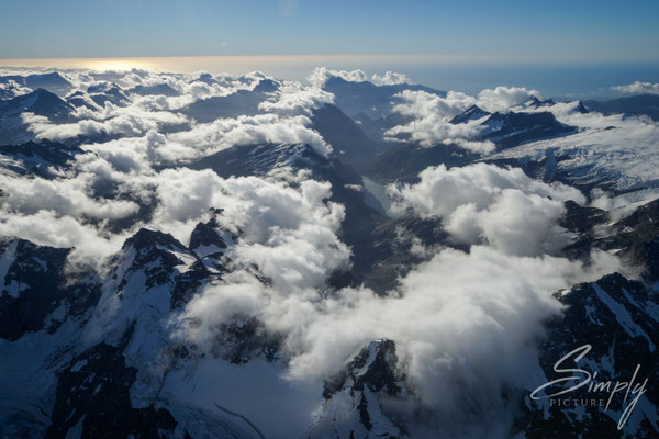 Flug über die südlichen Alpen, Wolkenmeer mit vielen Berggipfeln und dem Meer an dem Horizont