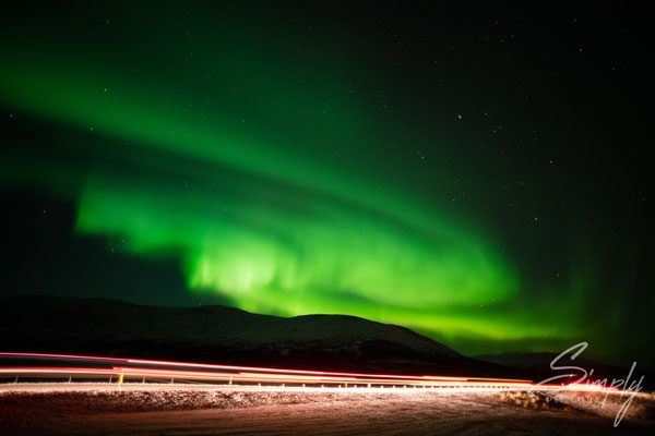 Grüne Aurora-Borialis mit Lichtern von vorbeifahrenden Autos bei Laugarvatn.