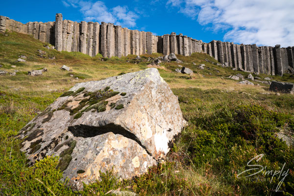 Gerðuberg Cliffs mit blauem Himmel und grünem Gras.