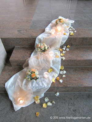Kirchenschmuck auf den Stufen zum Altar: Satin- und Organzastoff drapiert, kleine Bouqets, Windlichter und gestreute Rosenblütenblätter