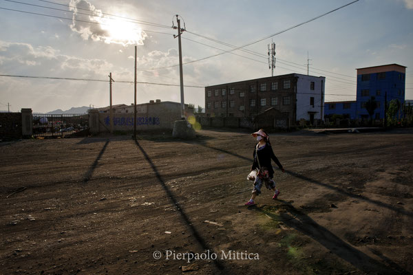 pedestrian with a mask to protect herself by the pollution, on the road to the coal mines, in the semi-evacuated town of Gongwusu